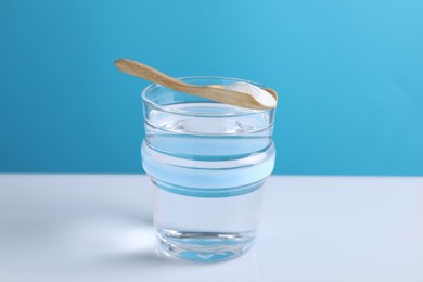 Glass of water and spoon with baking soda on color background