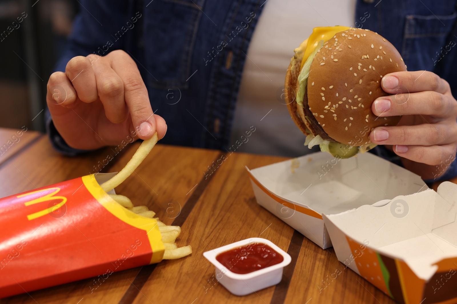 Photo of Lviv, Ukraine - October 9, 2023: Woman with McDonald's menu at wooden table in restaurant, closeup