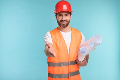 Photo of Architect in hard hat with drafts greeting someone on light blue background