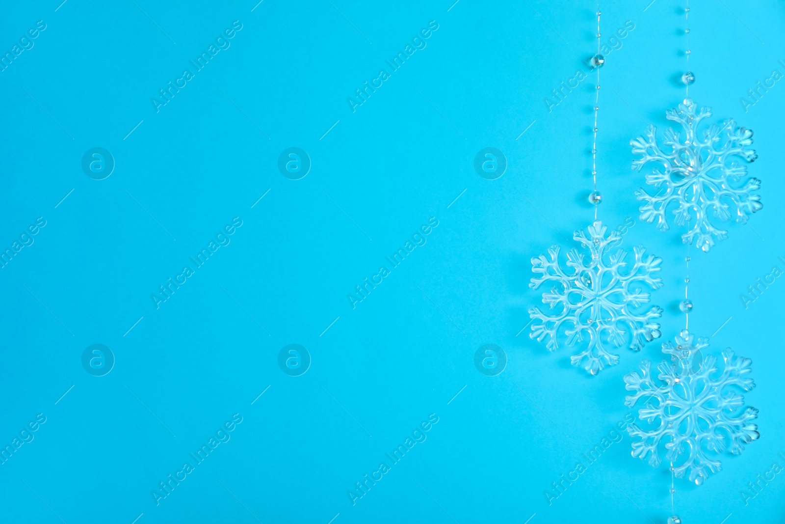 Photo of Beautiful decorative snowflakes hanging on light blue background, space for text