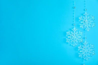 Photo of Beautiful decorative snowflakes hanging on light blue background, space for text