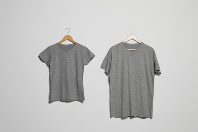 Photo of Hangers with different t-shirts on light wall. Mockup for design