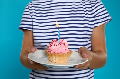 Photo of Happy boy holding birthday cupcake with candle on blue background, closeup