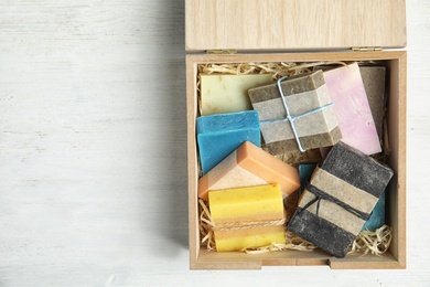 Different handmade soap bars in wooden box and space for text on table, top view