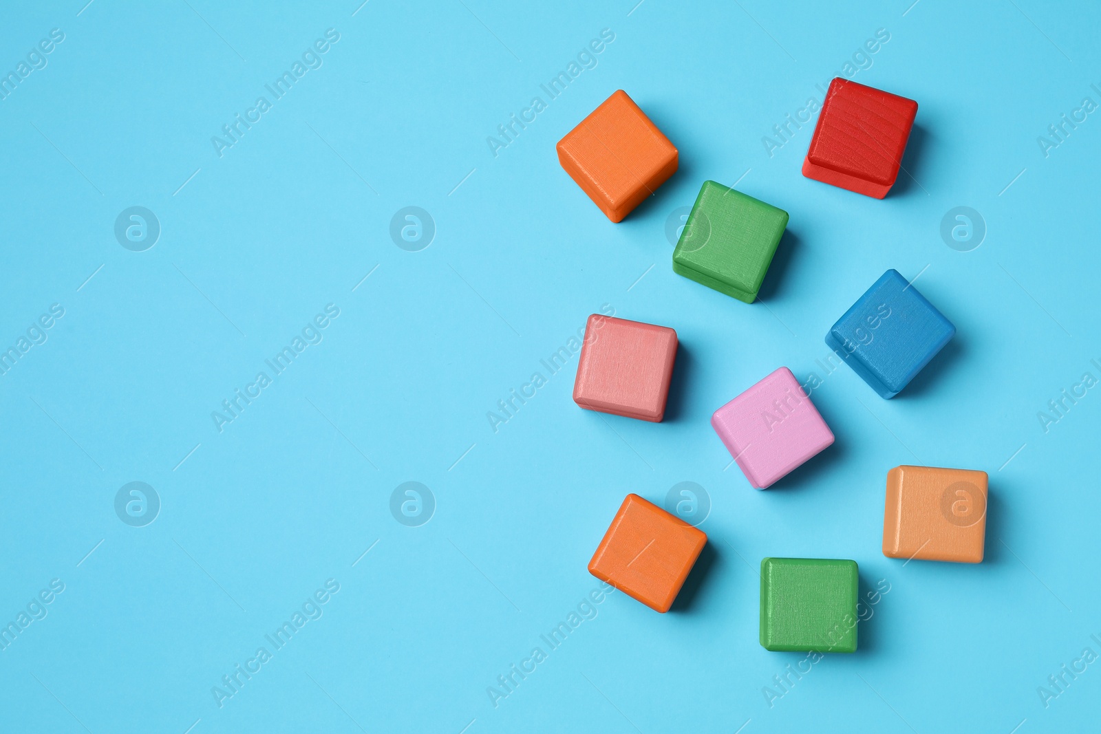 Photo of Blank colorful cubes on light blue background, flat lay. Space for text