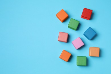 Photo of Blank colorful cubes on light blue background, flat lay. Space for text