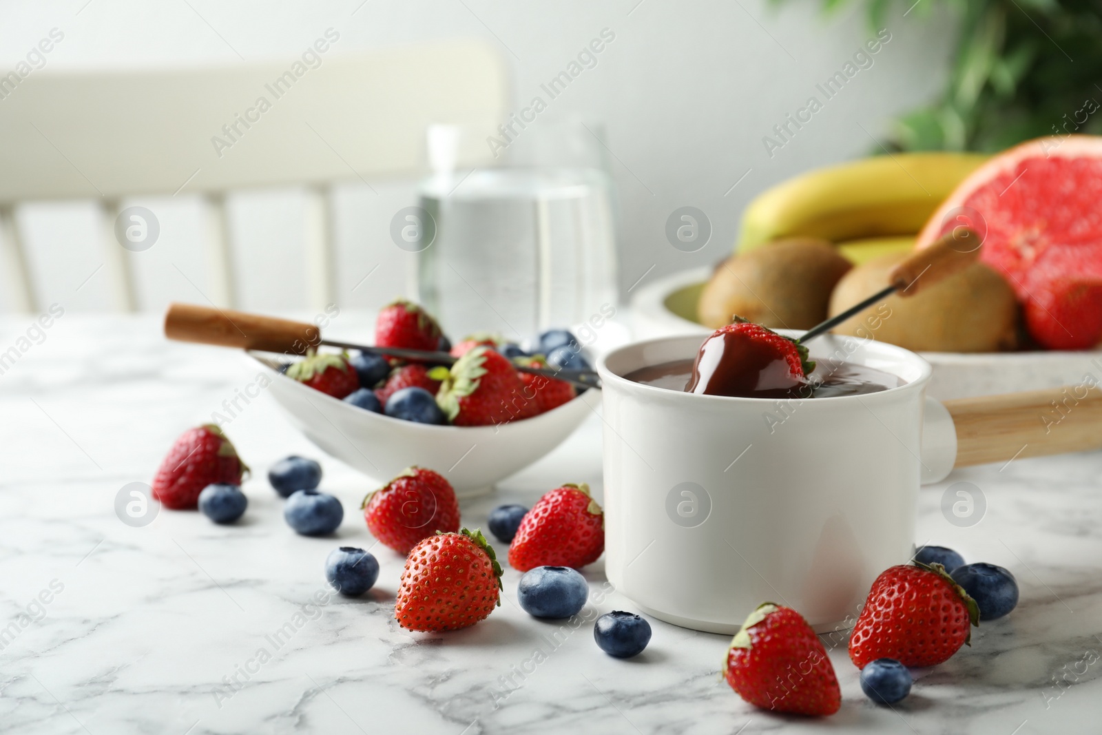 Photo of Fondue pot with chocolate and fresh berries on white marble table