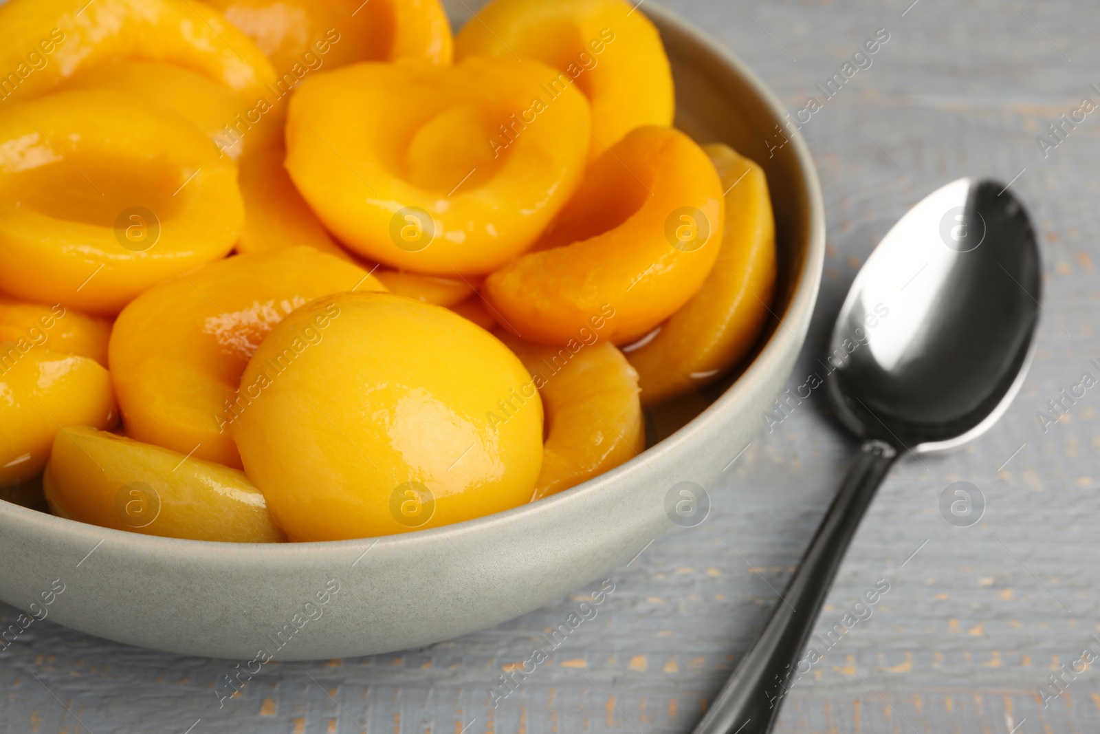 Photo of Canned peach halves and spoon on grey wooden table, closeup