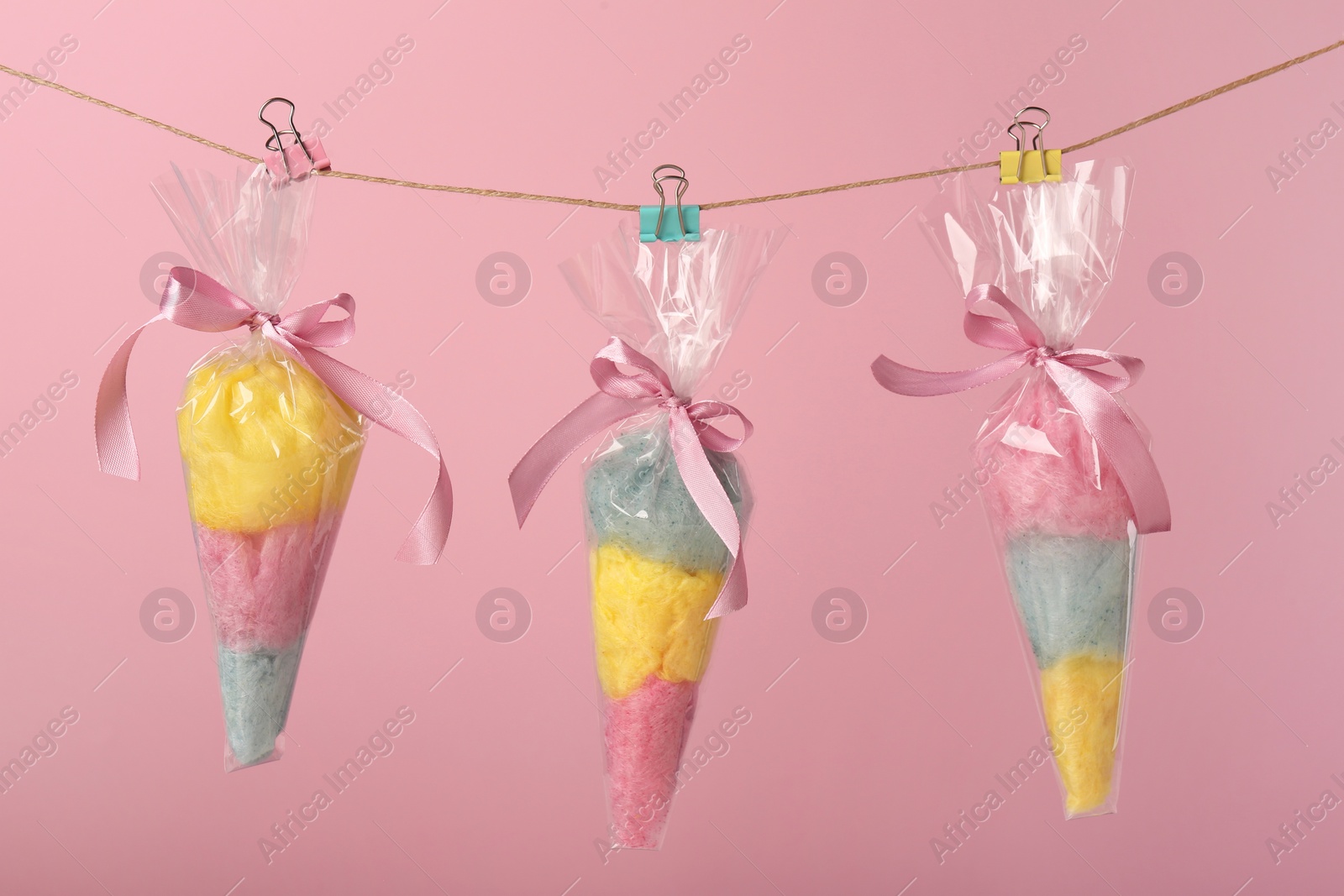 Photo of Packaged sweet cotton candies hanging on clothesline against pink background