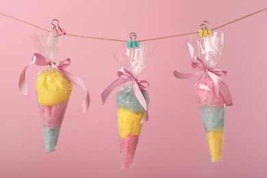 Photo of Packaged sweet cotton candies hanging on clothesline against pink background