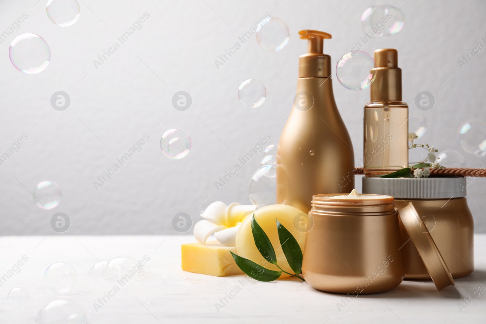 Photo of Set of hair cosmetic products, flowers and soap bubbles on grey background. Space for text