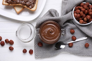 Photo of Jar with chocolate paste, tasty toast and nuts on white wooden table, flat lay