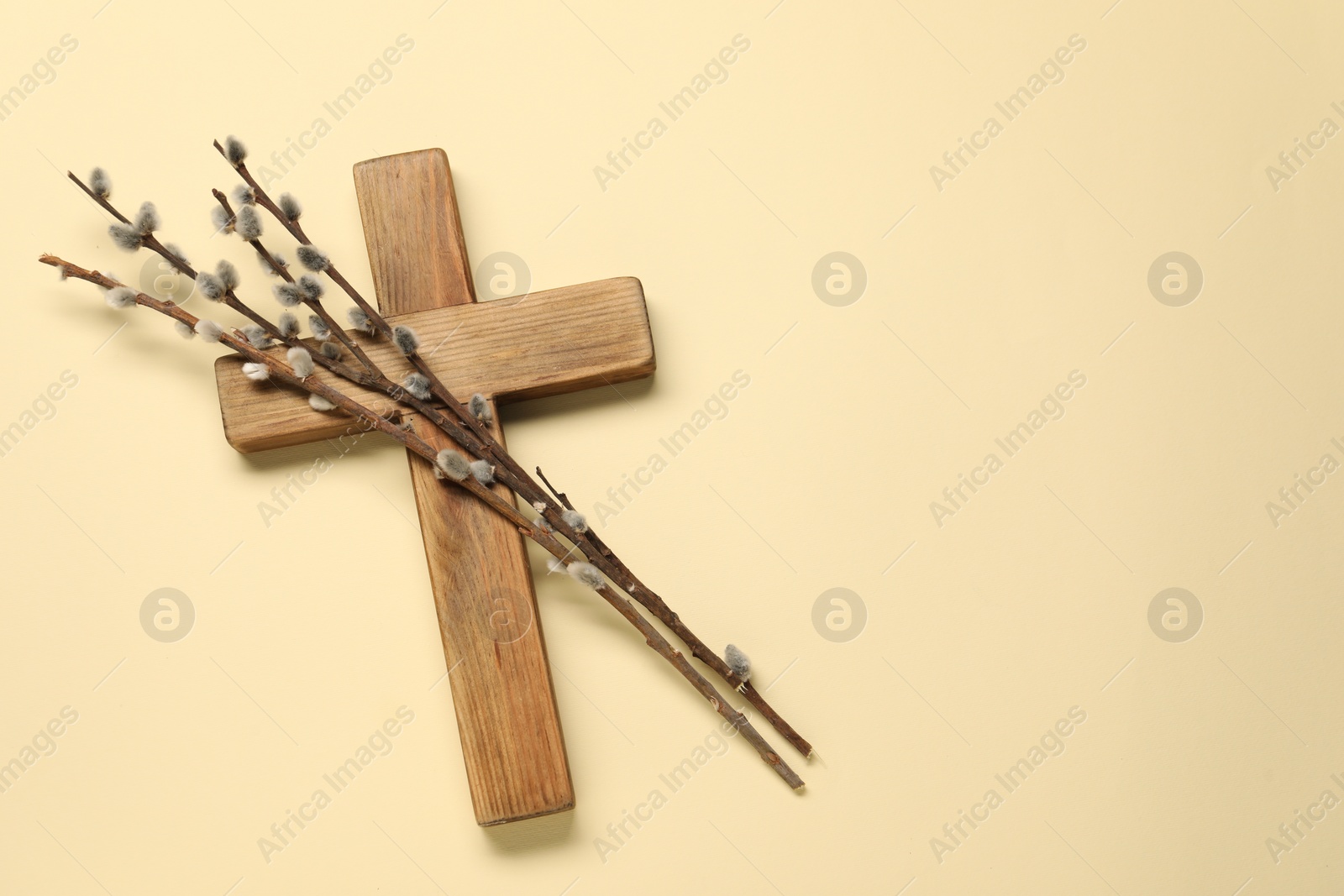 Photo of Wooden cross and willow branches on beige background, top view with space for text. Easter attributes