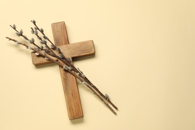 Wooden cross and willow branches on beige background, top view with space for text. Easter attributes