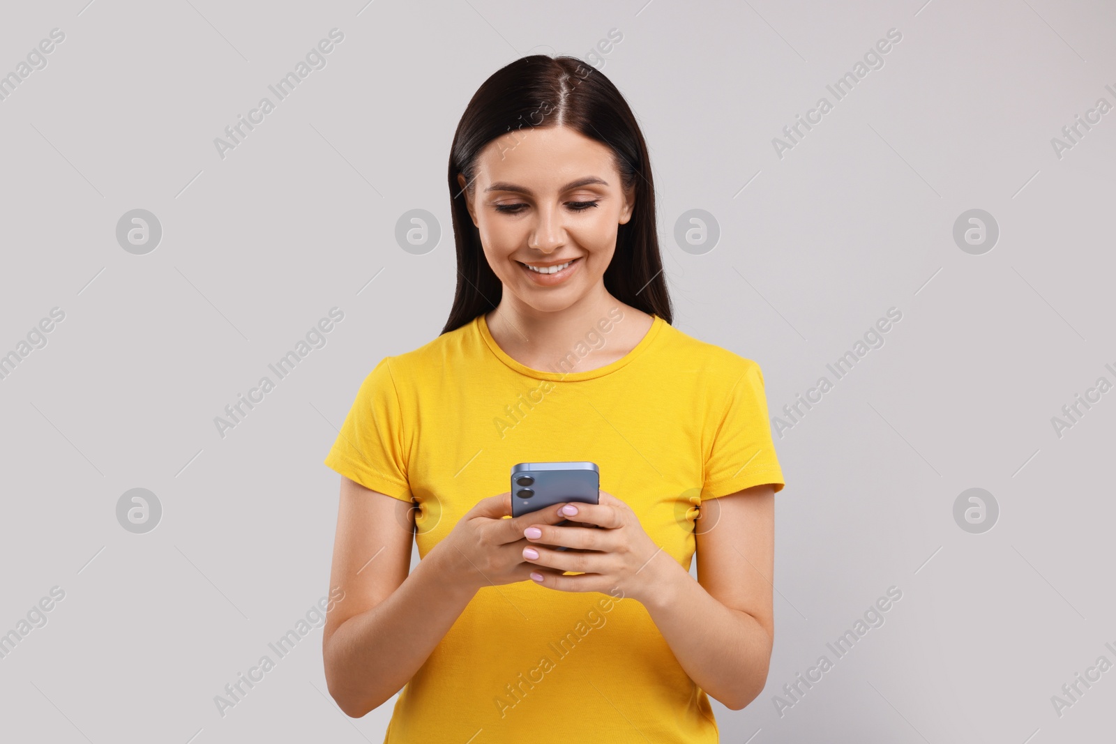 Photo of Young woman using smartphone on grey background