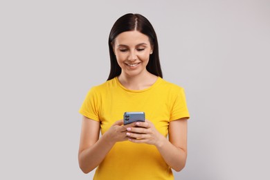 Young woman using smartphone on grey background