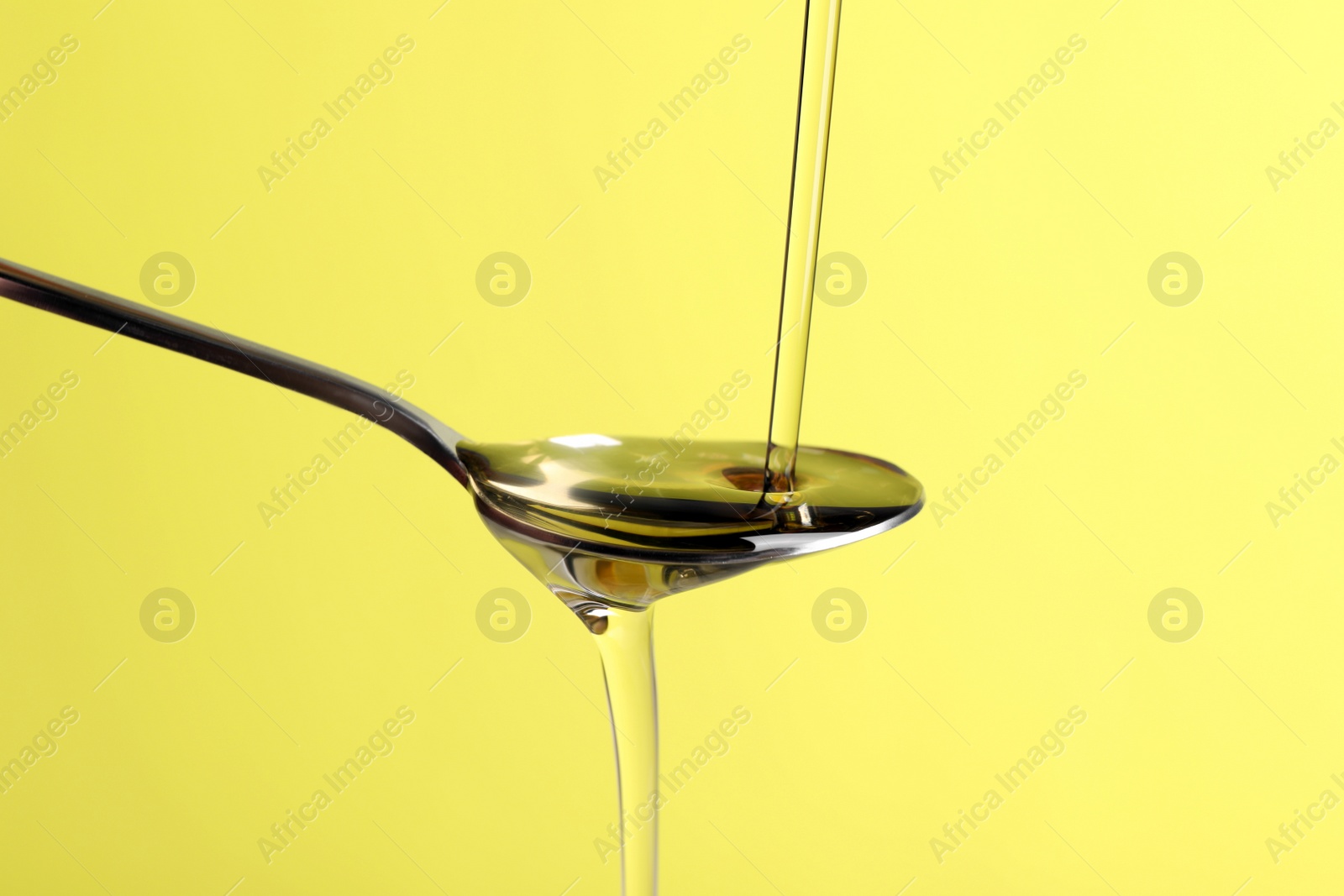 Photo of Pouring cooking oil into spoon on yellow background, closeup