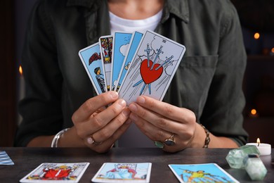 Photo of Fortune teller with tarot cards at grey table indoors, closeup
