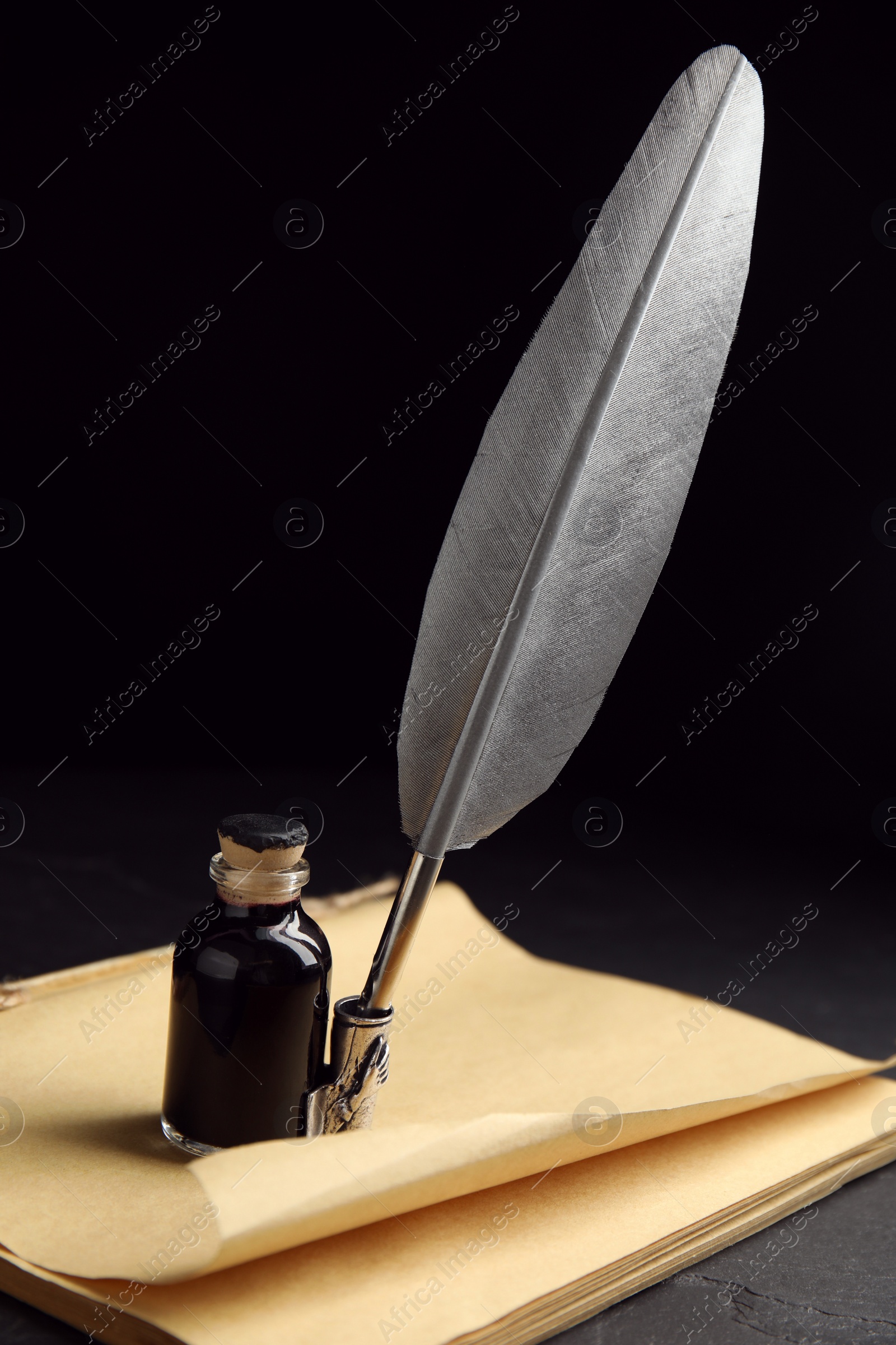 Photo of Feather pen, bottle of ink and old paper on black table