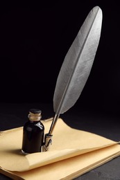 Feather pen, bottle of ink and old paper on black table