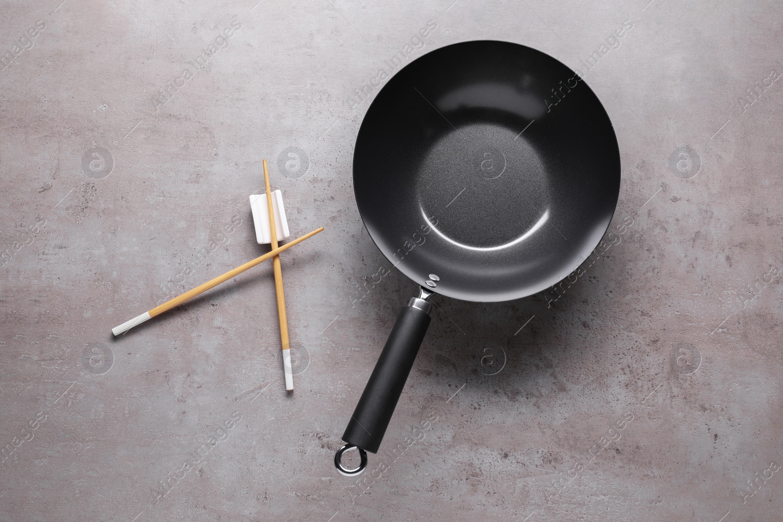 Photo of Empty iron wok and chopsticks on grey table, flat lay