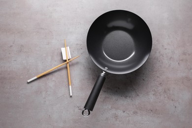 Empty iron wok and chopsticks on grey table, flat lay