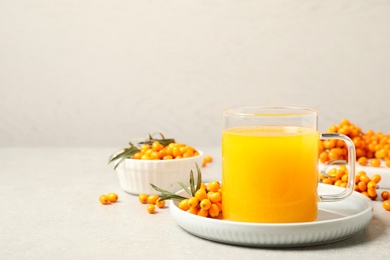 Photo of Delicious sea buckthorn tea and fresh berries on light grey table. Space for text