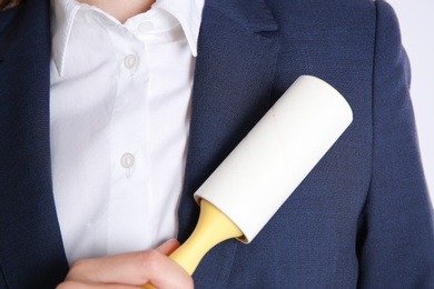 Woman cleaning dark blue jacket with lint roller, closeup