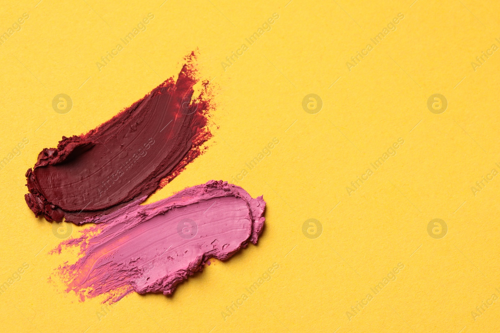 Photo of Smears of bright lipsticks on yellow background, top view. Space for text