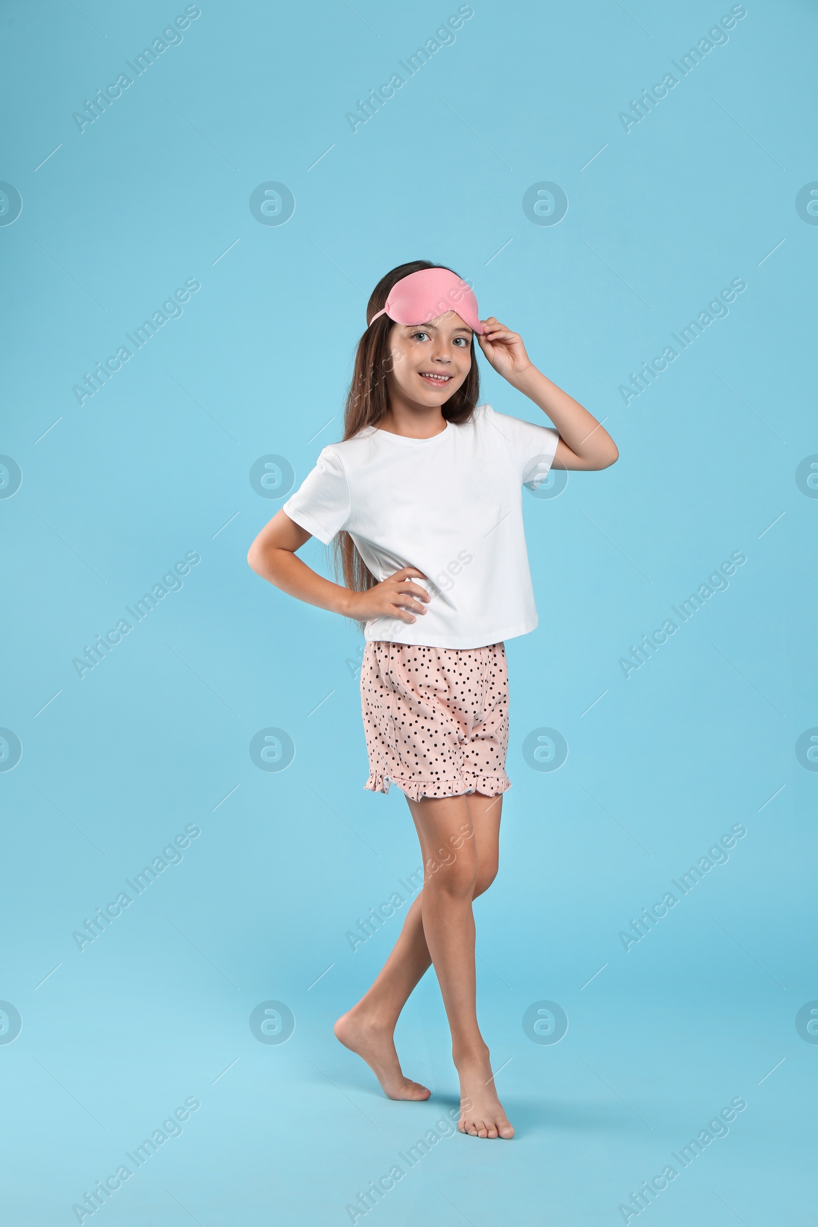 Photo of Cute girl wearing pajamas and sleeping mask on light blue background