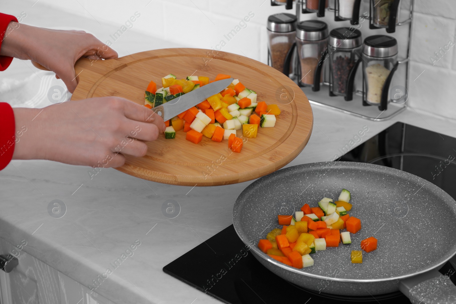 Photo of Woman putting cut vegetables onto frying pan in kitchen, closeup