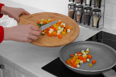Woman putting cut vegetables onto frying pan in kitchen, closeup