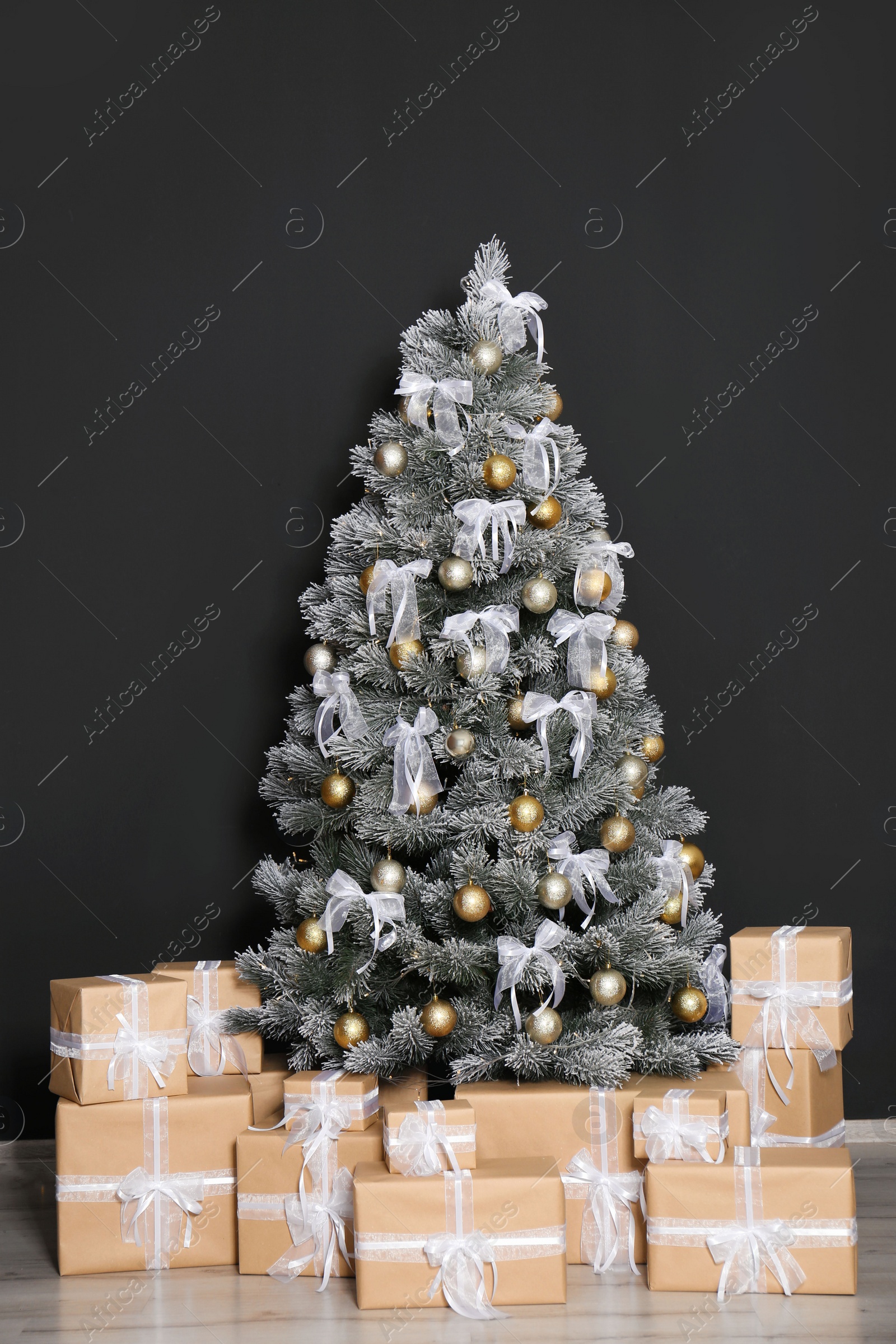 Photo of Decorated Christmas tree and gift boxes near black wall