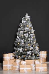 Decorated Christmas tree and gift boxes near black wall