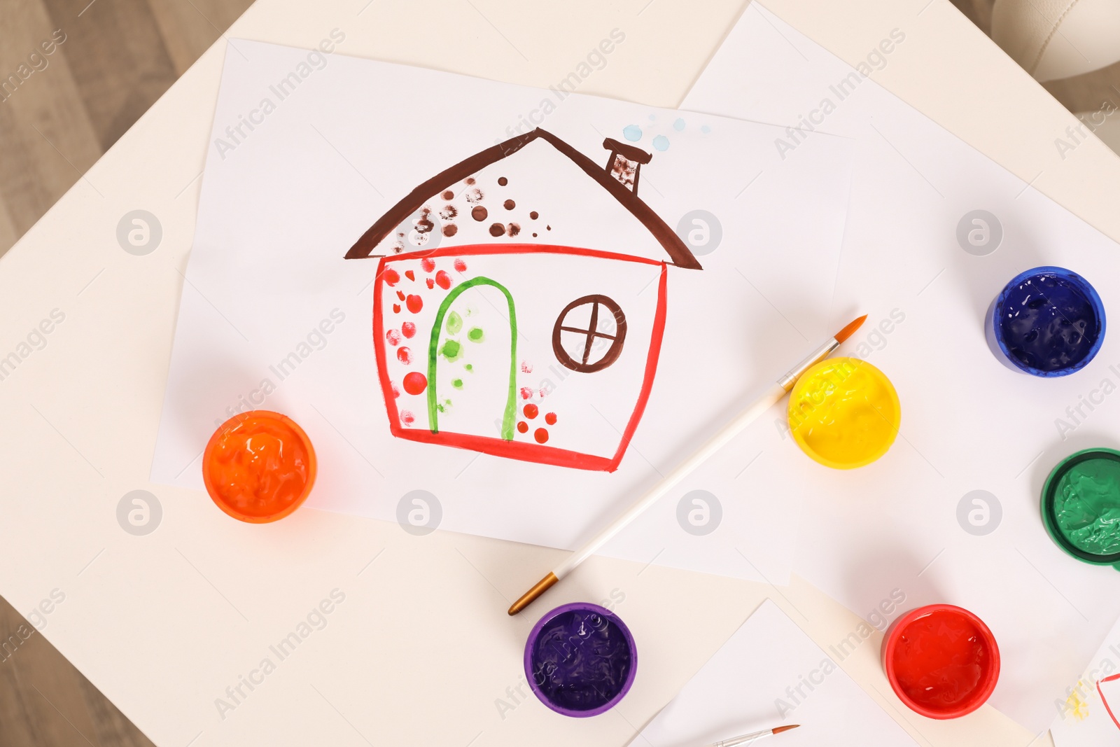 Photo of Cute children's drawing, brushes and set of paints on white table, flat lay