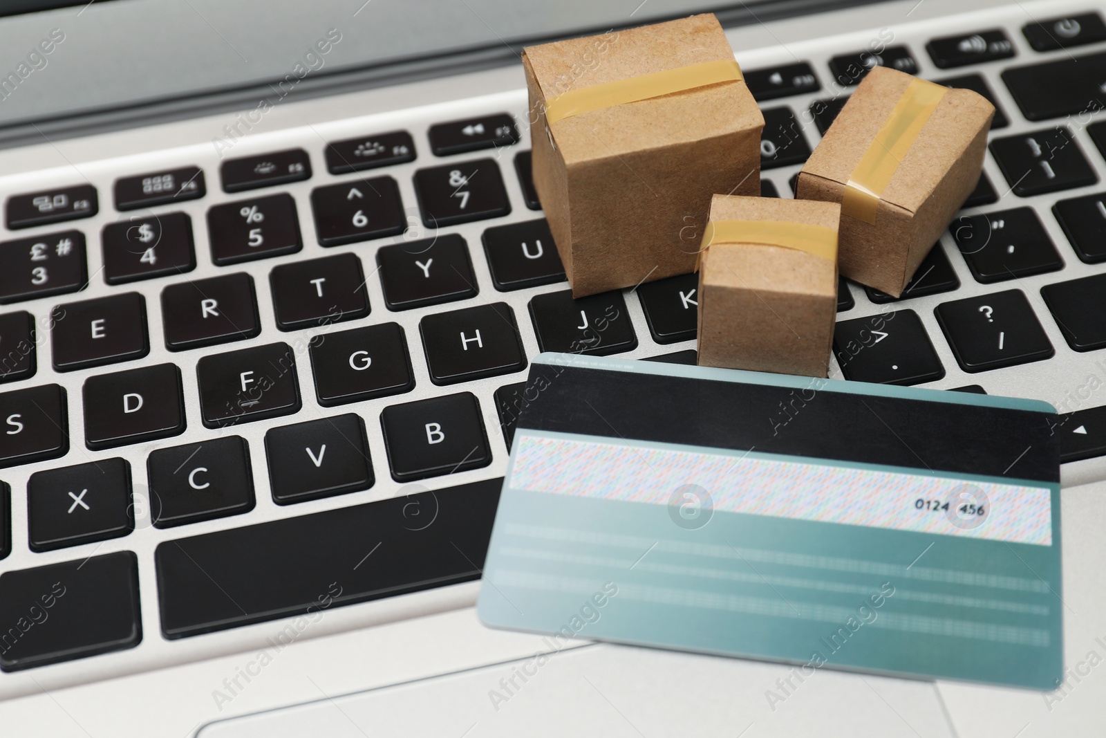 Photo of Internet shopping. Small cardboard boxes and credit card on laptop, closeup. Space for text