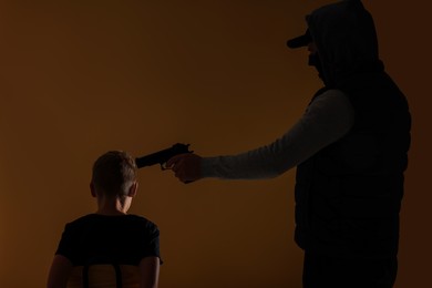Kidnapper pointing gun at little boy taken hostage on dark background