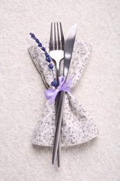 Photo of Cutlery, napkin and preserved lavender flower on white textured table, top view