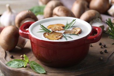 Photo of Delicious homemade mushroom soup in ceramic pot and fresh ingredients on wooden table