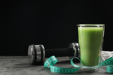 Photo of Tasty shake, dumbbell and measuring tape on grey table against black background, space for text. Weight loss
