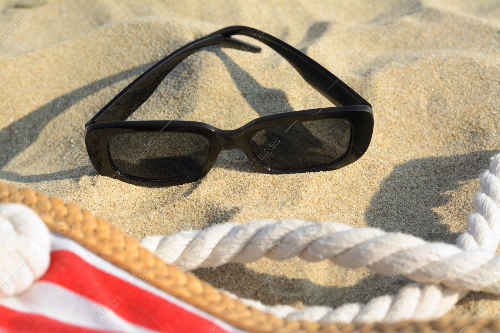 Photo of Stylish sunglasses and beach bag on sand, closeup