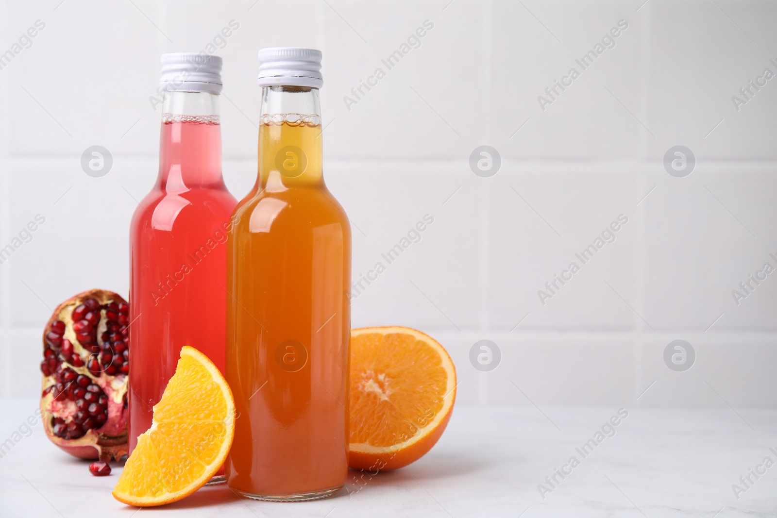 Photo of Delicious kombucha in glass bottles, pomegranate and orange on white table, space for text