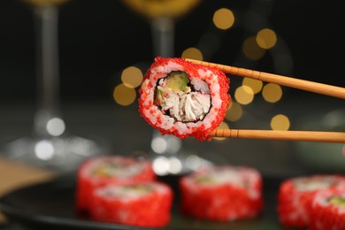 Photo of Chopsticks and delicious sushi roll against blurred lights, closeup