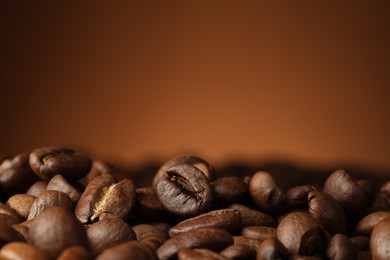 Photo of Heap of aromatic roasted coffee beans on brown background, closeup