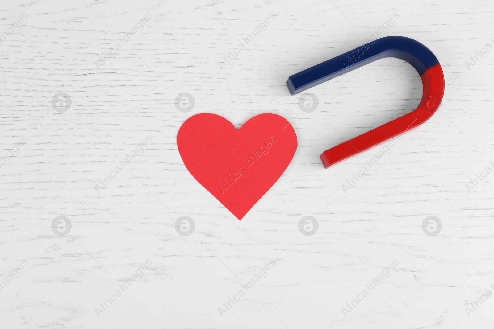 Photo of Red and blue horseshoe magnet and paper heart on white wooden table, flat lay