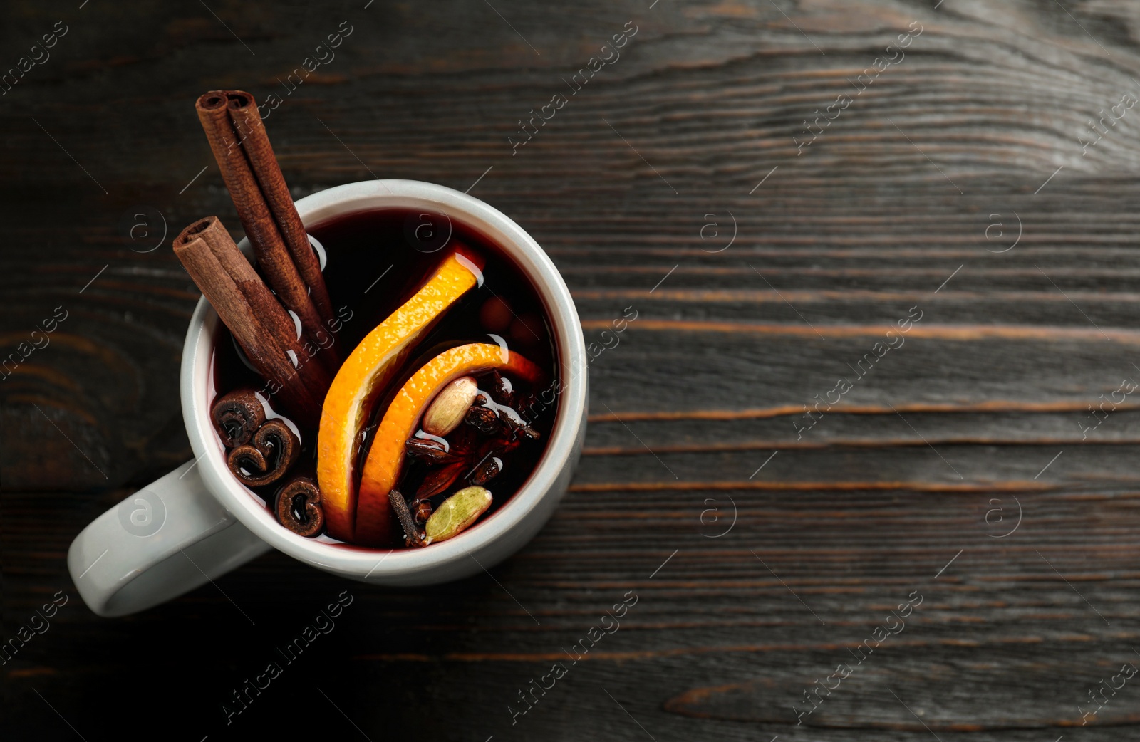 Photo of Cup of tasty mulled wine on black wooden table, top view. Space for text