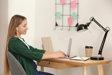 Photo of Teenage girl working on laptop at wooden desk in room