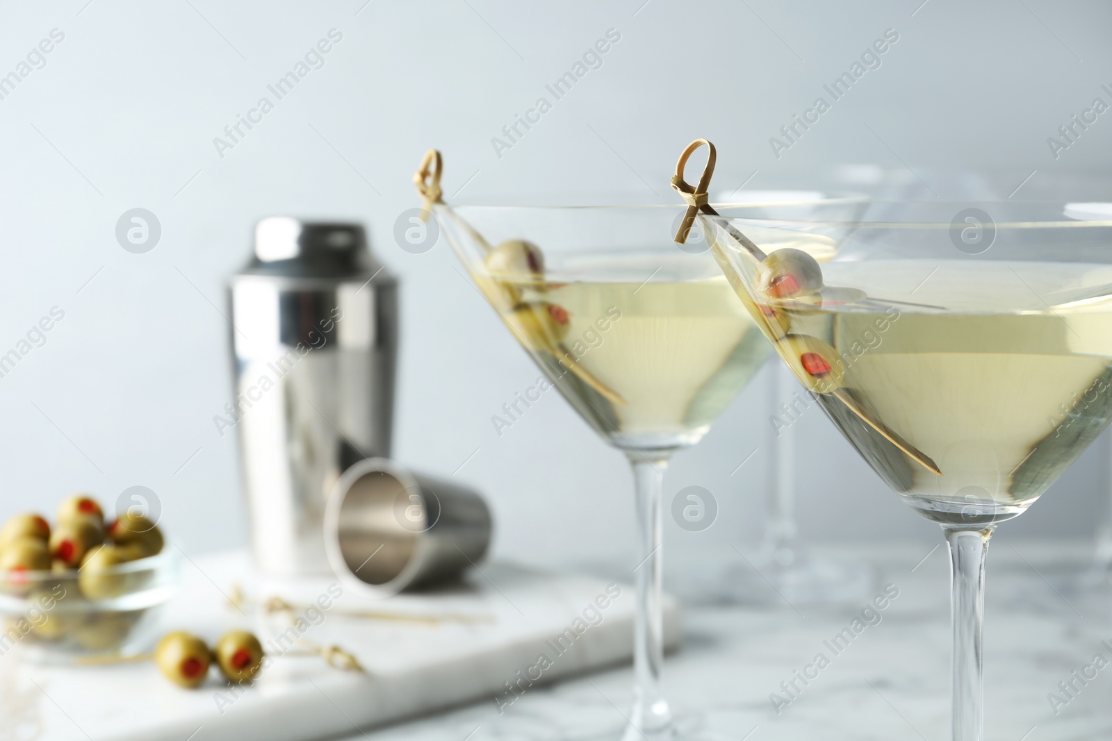 Photo of Glasses of Classic Dry Martini with olives on white marble table against grey background