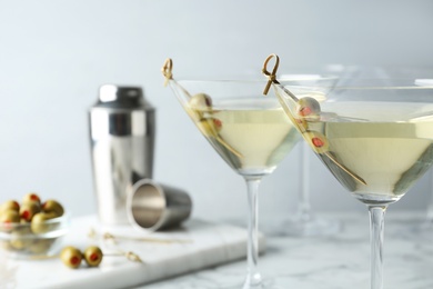 Glasses of Classic Dry Martini with olives on white marble table against grey background