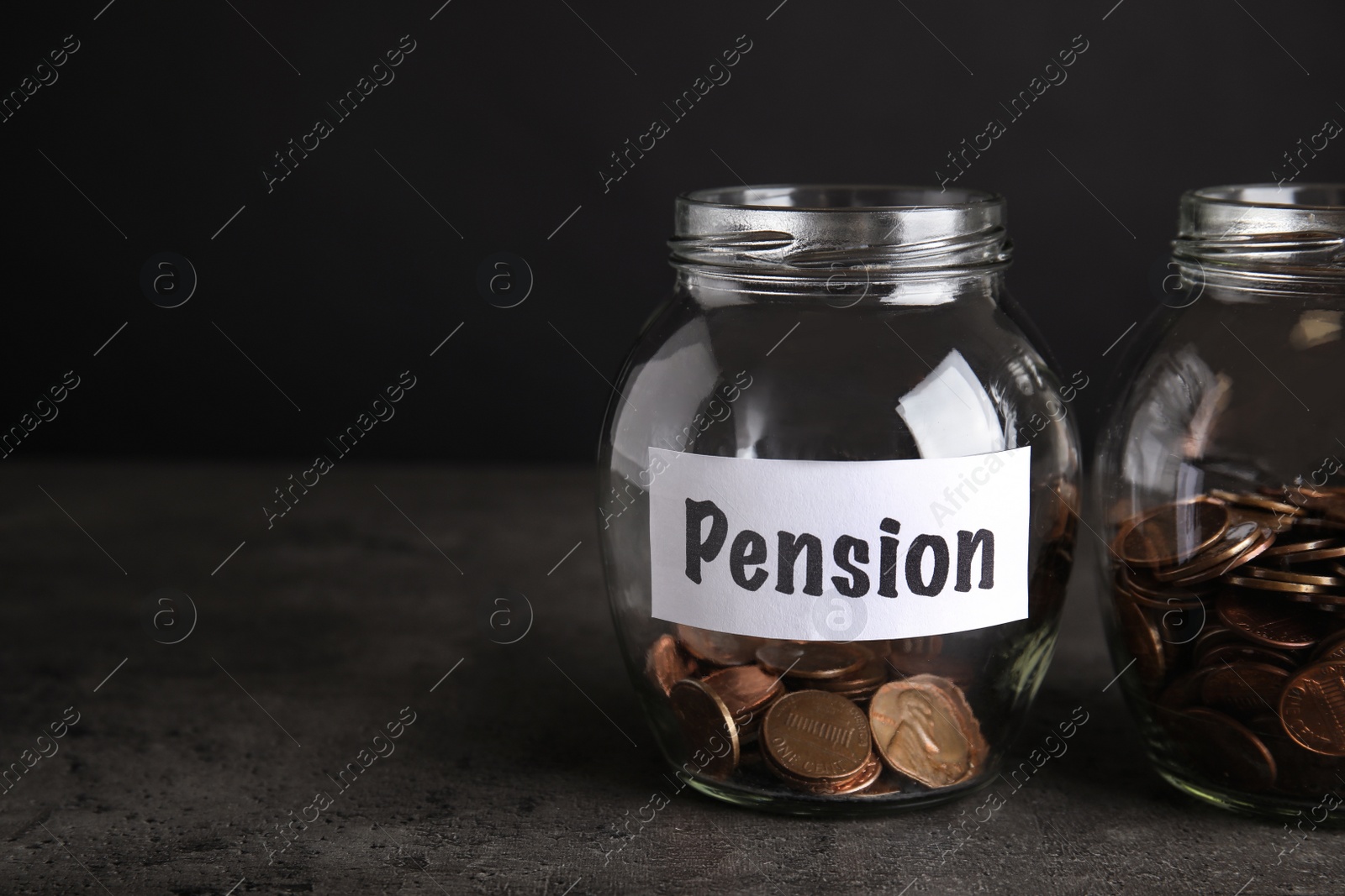 Photo of Glass jars with coins and label PENSION on dark table. Space for text